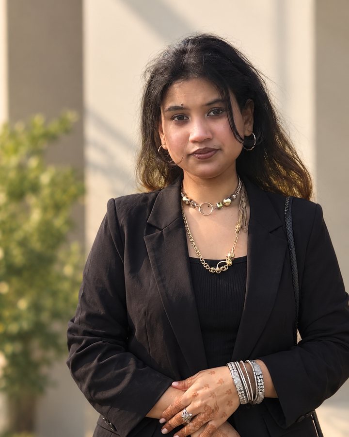 Portrait of Tanha Asfika Jaman wearing a black blazer, standing outdoors in warm afternoon light